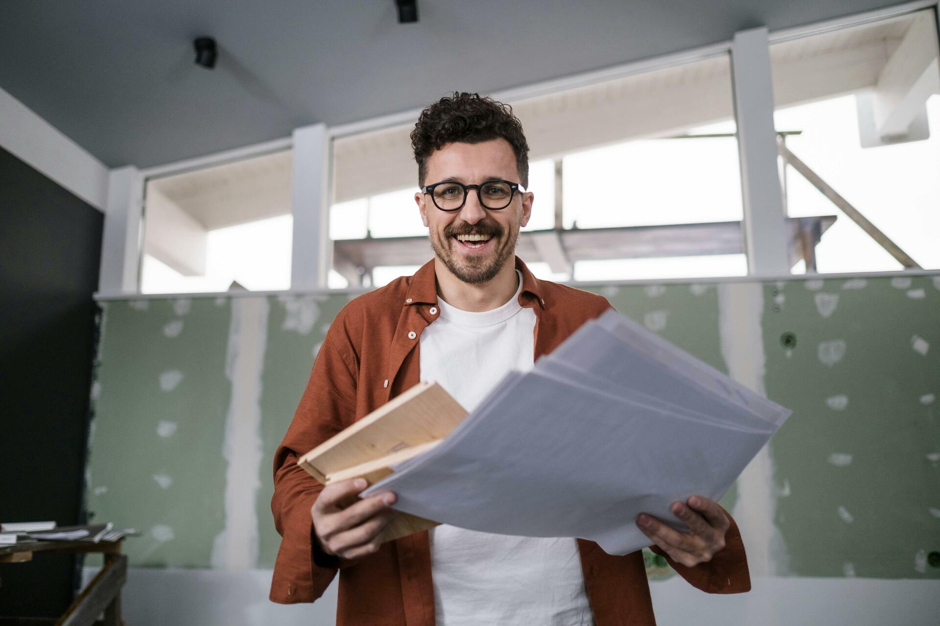 smiling-interior-designer-holding-plans-in-a-partially-renovated-room-conveying-excitement-and-creativity